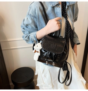 Glossy black mini bucket backpack with plush bear charm worn by model in denim jacket
