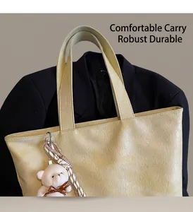 Close-up of cream yellow tote bag showing embossed PU leather texture and plush bear charm