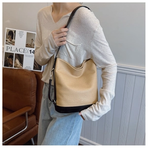 Detail of woven bucket bag with leather base and adjustable shoulder strap worn by model