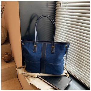 Detail of blue denim tote bag with leather strap and white stitching on books