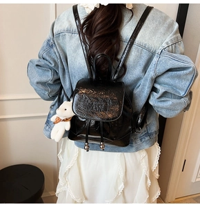 Detail of glossy black mini backpack with drawstring closure and white plush bear charm