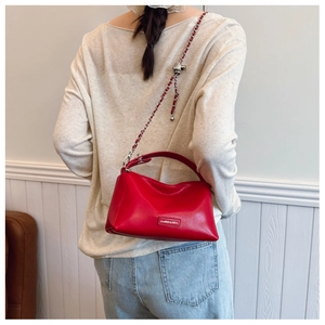 Detailed view of red crossbody bag with silver chain strap and metal logo tag