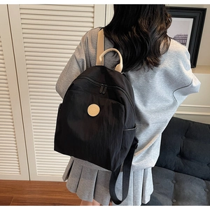 Detail of a black nylon travel backpack showing a round patch and brown top handle