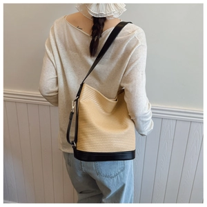 Detail of woven straw bucket bag with black leather trim and adjustable shoulder strap