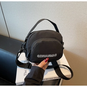 Detail of a small black nylon crossbody bag with dual zipper pockets and top handle