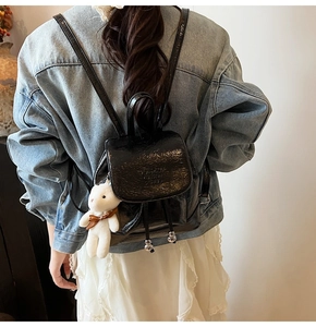 Close-up of black glossy patent leather bucket backpack with bear charm and ribbon detail