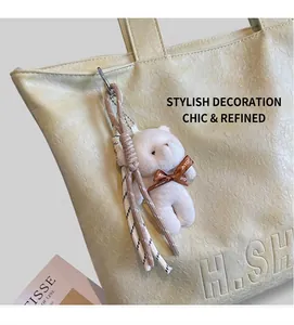 Detail of light yellow leather tote bag featuring H.SH relief logo and plush bear charm