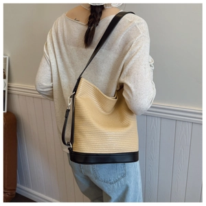 Detail of a woven straw bucket bag with black leather strap and base on a female model