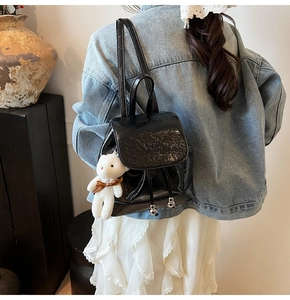 Detail of black glossy bucket backpack with drawstring and plush bear charm on model