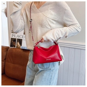 Detail of red pebbled leather bag with woven chain strap and metallic logo plaque