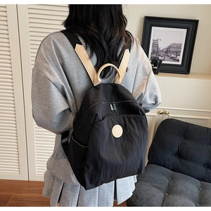 Detail of black mini nylon backpack showing beige contrast straps and a secure double zipper