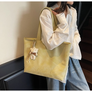 Close-up of lime yellow leather tote bag featuring H.SHAN logo and cute plush bear charm
