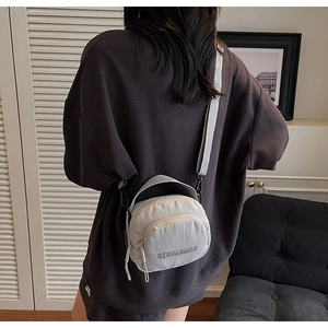 Back view of a model wearing a light grey nylon mini crossbody bag with top handle