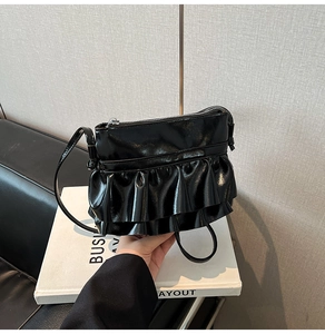 Detail of black ruffled crossbody bag with glossy finish and silver zipper closure