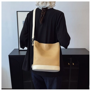 Detail of hand-woven straw bucket bag with white leather trim worn as a shoulder bag