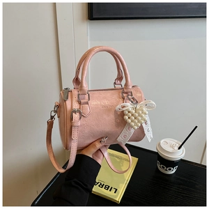Sac cylindrique rose avec breloque perle en cœur et ruban dans un décor lifestyle