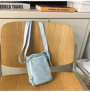 Light blue nylon crossbody bag with adjustable shoulder strap hanging on a wooden chair