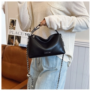Detail of black leather shoulder bag with silver chain and brand nameplate on sofa