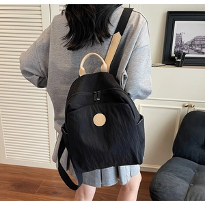 Detail of a lightweight black nylon backpack with beige handles and round logo patch