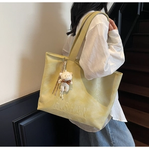 Detail of light green tote bag featuring H.SHAN embossed logo and white bear charm