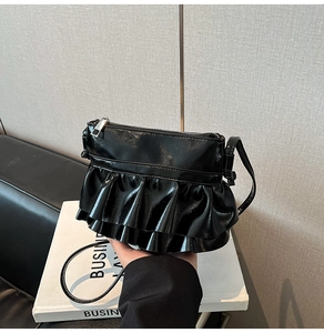 Detail of black glossy leather handbag with layered ruffle design and silver zipper closure