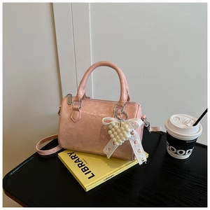 Détail du sac cylindrique en cuir verni rose avec breloque cœur perle et nœud
