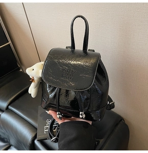 Detail of black glossy bucket backpack with drawstring and plush bear accessory