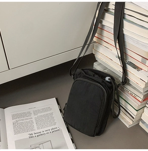 Detailed view of black nylon crossbody phone bag with adjustable strap on a minimalist desk