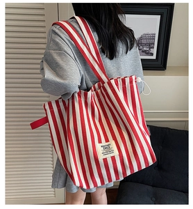 Detail showing red and white striped canvas tote bag with woven logo patch and dual straps
