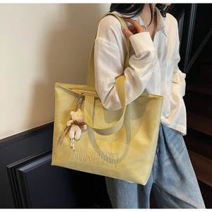 Detail of yellow tote bag with H.SHAN embossing and a cute plush bear charm on the strap