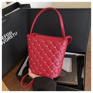 Dettaglio della borsa a secchiello rossa trapuntata con borchie su sfondo di scatola regalo