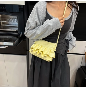 Detail of light yellow ruffle crossbody bag in patent leather worn by model in a modern room