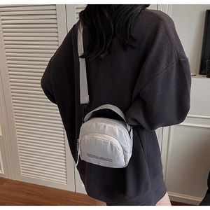 Light grey canvas crossbody bag worn by model against a minimalist white door background