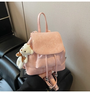 Close-up of pink pleated mini backpack with a plush bear charm and embossed text