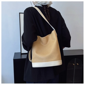 Detail of woven straw bucket bag with white leather straps worn over a black blazer