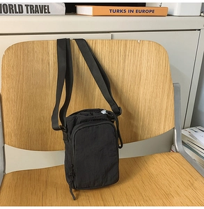 Detail of black nylon crossbody bag with double zippers hanging on a wooden chair
