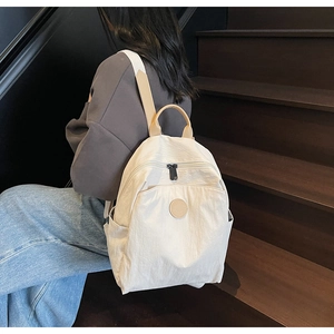 Close-up of lightweight off-white nylon backpack with leather handles on a female model