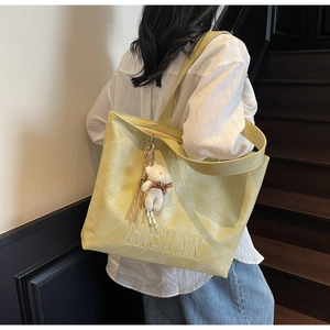 Detail of light yellow tote bag featuring pleated texture and cute bear pendant