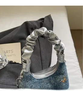 Dettaglio borsa a mezzaluna in denim con fibbia a farfalla di strass e manico metallico
