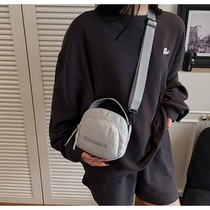 Close-up of a light grey nylon crossbody bag with adjustable strap on a model