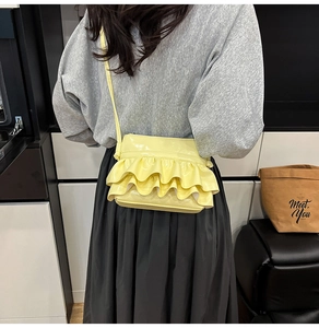 Detail view of yellow ruffled crossbody bag with glossy finish on a stylish model