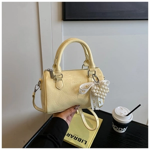 Détail du sac boston jaune avec texture plissée et pendentif cœur en perles