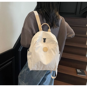 Back view of a model wearing a minimalist beige nylon backpack on wooden stairs