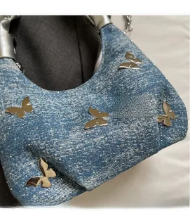 Dettaglio della borsa in denim blu con farfalle argentate e decorazioni in strass