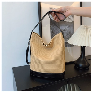 Close-up of woven tote bag with contrast black leather base and strap in a minimalist room