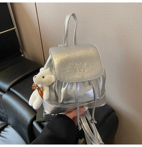 Detail of silver metallic backpack with drawstring, flap closure and plush bear charm