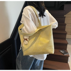 Detail view of light yellow tote bag with H.SHAN embossing and a cute bear charm
