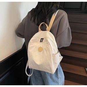 Outdoor side view of lightweight beige nylon backpack with brown straps and side pockets