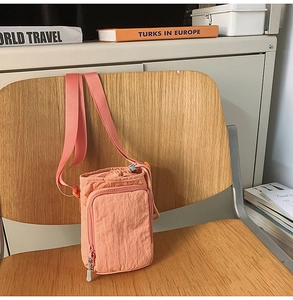 Detail of coral orange nylon crossbody bag with drawstring closure and front zipper pocket