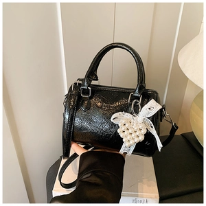 Gros plan du sac à main en cuir verni noir avec un charm cœur en dentelle et perles